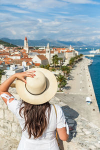 Rear view of woman standing on city walls looking at idyllic seaside town of trogir, croatia