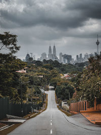 Road amidst trees and buildings against sky