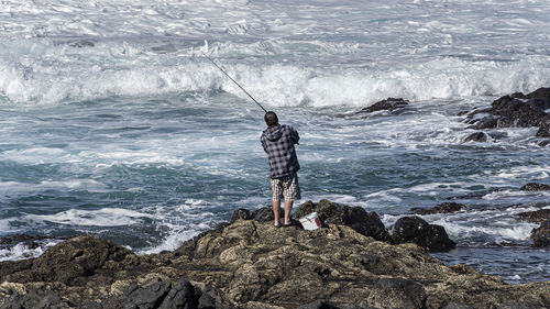 Rear view of man standing on rock in sea