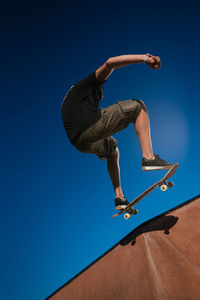 Low angle view of man skateboarding against clear blue sky