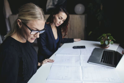 Female engineers looking at blueprint on desk in home office