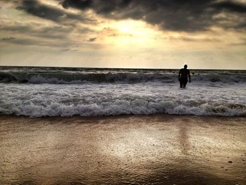 Silhouette man standing on shore in sea against sky during sunset