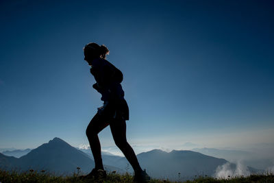 Low angle view of man standing on mountain against clear blue sky