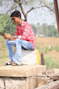 Full length of man using mobile phone while sitting outdoors