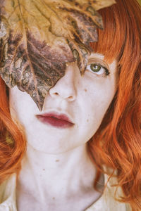 Portrait of woman with dry leaf standing against wall