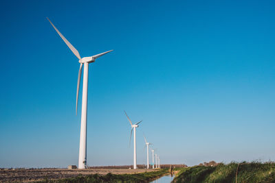 Windmill on field against clear blue sky