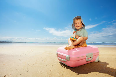 Portrait of young woman sitting on sand at beach against sky