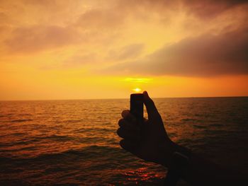 Silhouette hand against sea during sunset