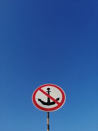 Low angle view of road sign against clear blue sky