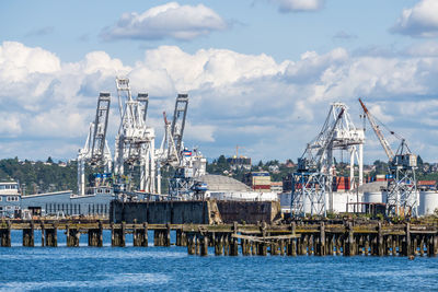 Cranes at harbor against cloudy sky