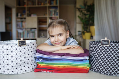 Portrait of smiling girl with folded clothes at home