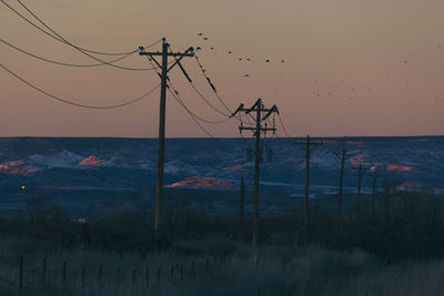 Scenic view of electricity poles against sky during sunset
