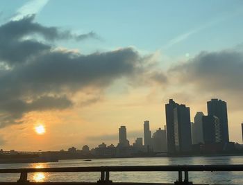 Scenic view of river by buildings against sky during sunset