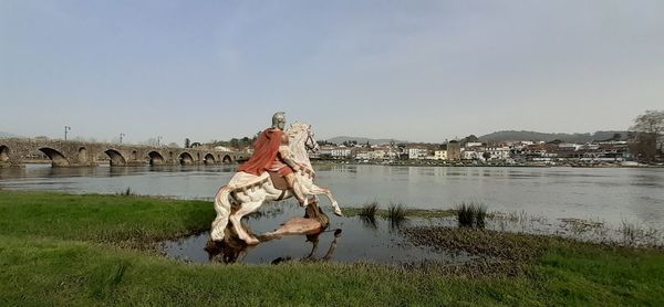 Horse statue by river in city against clear sky