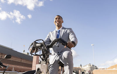 Happy businessman sitting on electric bicycle on sunny day