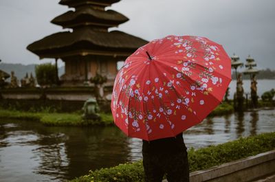 Close-up of woman with red umbrella standing in lake during rainy season