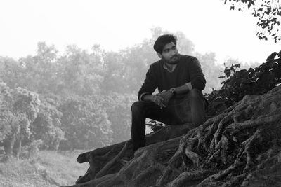 Man looking away while sitting by tree trunk