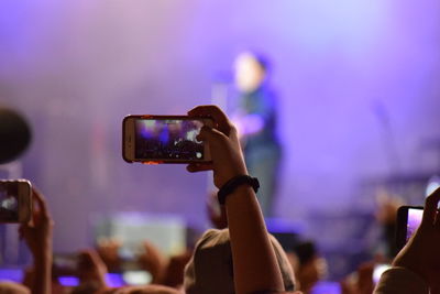 Cropped image of woman photographing musician on stage