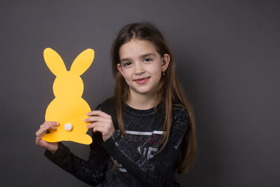 Portrait of smiling girl holding paper eater bunny against gray background