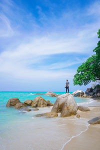 Man standing on rock by sea against sky