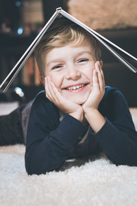 Portrait of smiling boy lying down with book on carpet