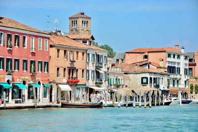 Boats in canal by buildings against sky