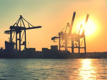 Silhouette cranes at commercial dock against sky during sunset