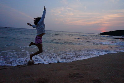 Man jumping on beach against sky during sunset