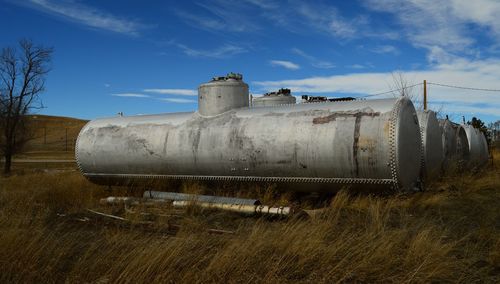 Storage tanks on grassy field against sky