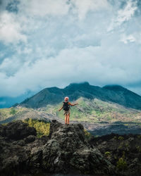 Man standing on rock looking at mountain against sky