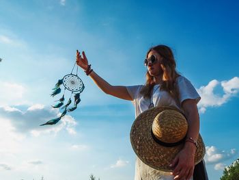 Woman holding dreamcatcher against sky