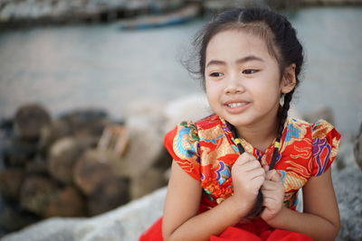 Cute girl looking away while sitting on rocks against sea