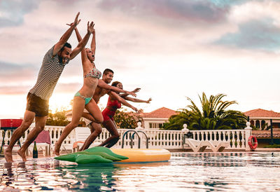 Friends jumping in swimming pool against sky