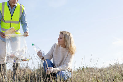 Woman looking at plastic bottle crouching by man