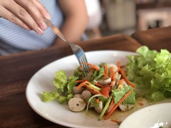 Midsection of person eating salad on wooden table at home