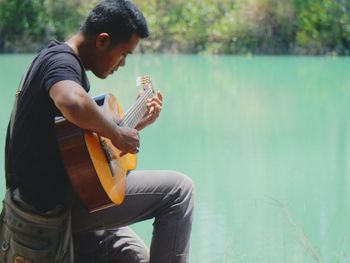 Side view of young man playing guitar by lake