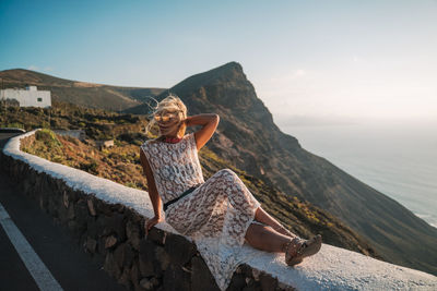 Full length of woman siting on retaining wall against valley