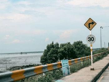 Road sign by railing against sky