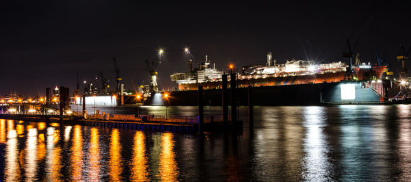 Illuminated harbor by sea against sky at night