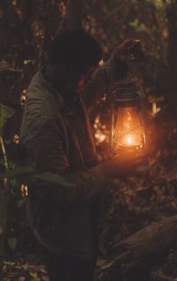 Rear view of man standing in forest lighting and oil lamp