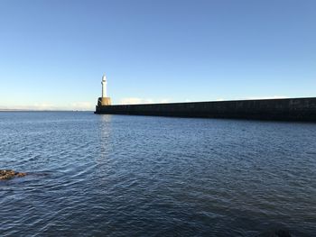 Lighthouse by sea against clear sky