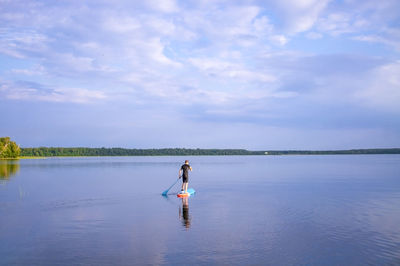 Man is paddling on a sup board on the lake. lake landscape and blue cloudy sky.