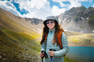 Smiling, positive girl with disheveled hair against the background of a blue mountain lake, with