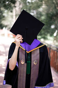 Woman holding mortarboard over face