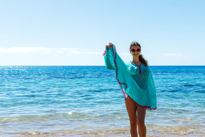 Full length of young woman standing in sea against sky