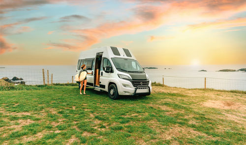 Woman with wetsuit and surfboard closing the door of her camper van to go surfing