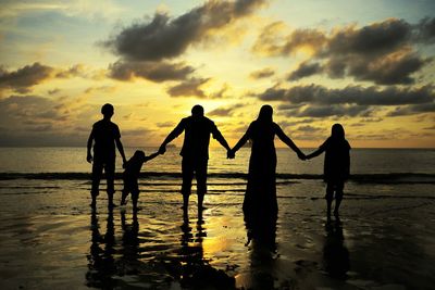 Rear view of silhouette family holding hands while standing on beach during sunset
