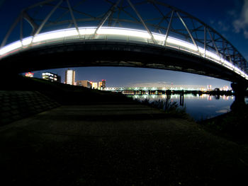 Bridge over river by illuminated buildings against sky at night
