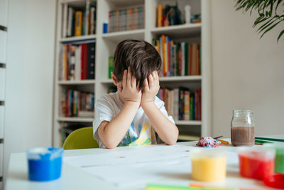 Tired boy sitting by table at home