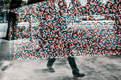 Double exposure of mosaic wall and low section of man walking on street